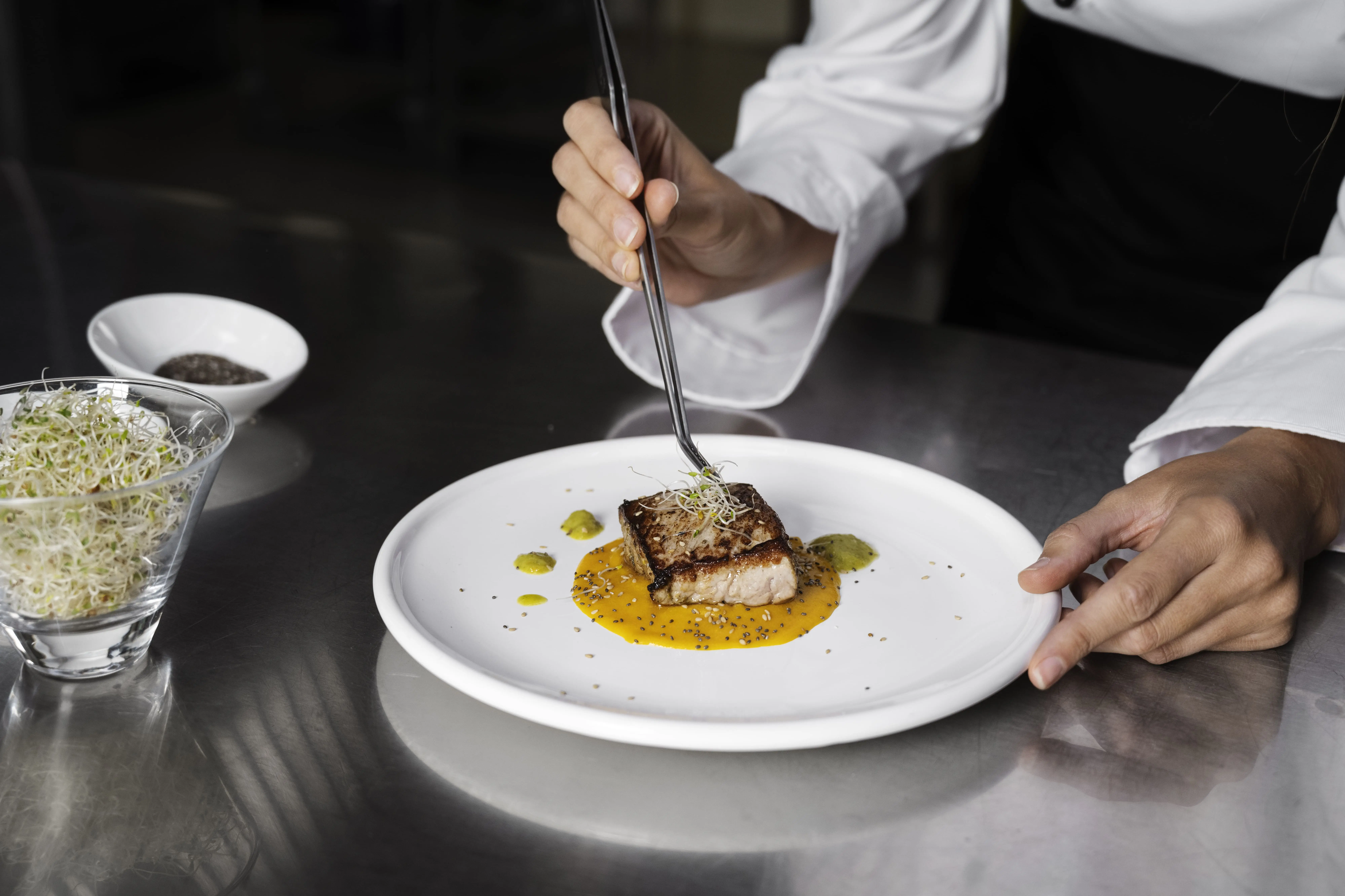 A kitchen staff plating a dish on a clean plate during peak hours at the restaurant.